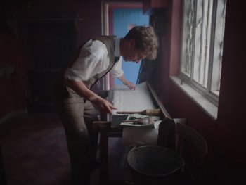 Movie still from “The Electrical Life of Louis Wain” (2021), directed by Will Sharpe – A man in a suit and tie is cutting paper; Medium shot, Low angle