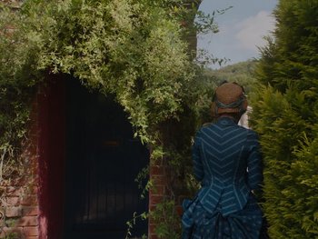 Movie still from “The Electrical Life of Louis Wain” (2021), directed by Will Sharpe – A woman in a blue dress standing next to a tree; Wide shot, Over the shoulder angle