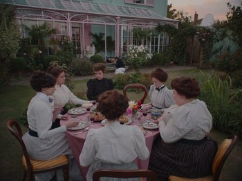 Movie still from “The Electrical Life of Louis Wain” (2021), directed by Will Sharpe – A group of people sitting around a table eating food; Wide shot, High angle