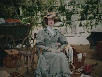 Movie still from “The Electrical Life of Louis Wain” (2021), directed by Will Sharpe – A woman sitting in a chair wearing a dress and a hat; Wide shot, High angle
