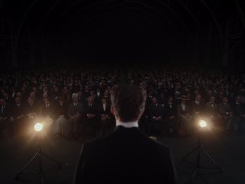 Movie still from “The Electrical Life of Louis Wain” (2021), directed by Will Sharpe – A man standing in front of a crowd of people at night; Extreme Wide shot, High angle