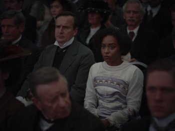 Movie still from “The Electrical Life of Louis Wain” (2021), directed by Will Sharpe – A group of people sitting next to each other in a room; Medium shot, Over the shoulder angle