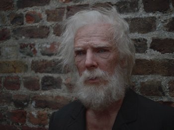 Movie still from “The Electrical Life of Louis Wain” (2021), directed by Will Sharpe – An old man with a white beard is standing in front of a brick wall; Close Up shot, High angle
