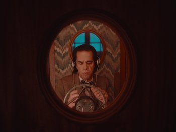 Movie still from “The Electrical Life of Louis Wain” (2021), directed by Will Sharpe – A man with headphones is sitting in a steering wheel; Medium shot, Overhead angle