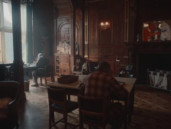 Movie still from “The Electrical Life of Louis Wain” (2021), directed by Will Sharpe – A group of people sitting at a table in a room; Wide shot, Over the shoulder angle