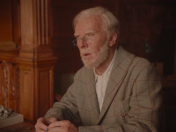 Movie still from “The Electrical Life of Louis Wain” (2021), directed by Will Sharpe – An old man with a beard and glasses is sitting at a table; Close Up shot, Over the shoulder angle