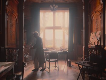 Movie still from “The Electrical Life of Louis Wain” (2021), directed by Will Sharpe – An old man standing in front of a chair in a living room; Wide shot, Low angle