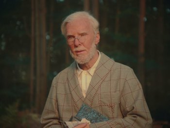Movie still from “The Electrical Life of Louis Wain” (2021), directed by Will Sharpe – An older man holding a book while standing in front of a forest; Medium shot, Over the shoulder angle