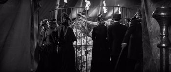 Movie still from “The Elephant Man” (1980), directed by David Lynch – A group of people standing next to each other in front of a fence; Wide shot, Low angle
