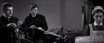 Movie still from “The Elephant Man” (1980), directed by David Lynch – A man holding a rope in a room; Medium shot, High angle