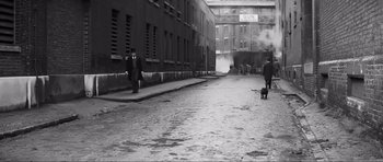 Movie still from “The Elephant Man” (1980), directed by David Lynch – A man walking a dog down a street; Extreme Wide shot, High angle