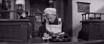 Movie still from “The Elephant Man” (1980), directed by David Lynch – An older woman writing on a piece of paper in front of a table; Medium shot, Low angle