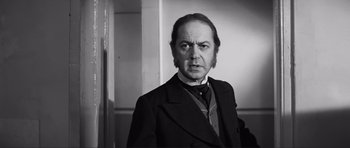Movie still from “The Elephant Man” (1980), directed by David Lynch – A man in a suit and tie standing in front of a wall; Close Up shot, Over the shoulder angle