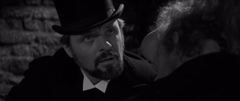 Movie still from “The Elephant Man” (1980), directed by David Lynch – A black and white photo of a man with a beard wearing a top hat; Close Up shot, Over the shoulder angle