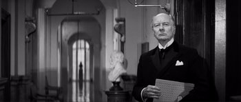 Movie still from “The Elephant Man” (1980), directed by David Lynch – An older man in a suit and tie holding a paper; Medium shot, Low angle