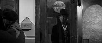 Movie still from “The Elephant Man” (1980), directed by David Lynch – A black and white photo of a man in a suit and hat; Medium shot, Low angle