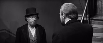 Movie still from “The Elephant Man” (1980), directed by David Lynch – A man wearing a top hat looking at another man in a suit; Medium shot, Over the shoulder angle