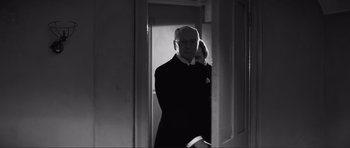 Movie still from “The Elephant Man” (1980), directed by David Lynch – An older man standing in a doorway holding a cell phone to his ear; Medium shot, Over the shoulder angle
