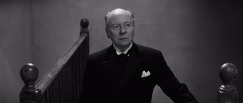 Movie still from “The Elephant Man” (1980), directed by David Lynch – An older man in a suit standing in front of a stair railing; Close Up shot, Low angle