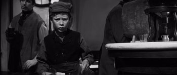 Movie still from “The Elephant Man” (1980), directed by David Lynch – A young boy sitting in front of a wooden chair; Medium shot, High angle