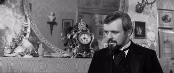 Movie still from “The Elephant Man” (1980), directed by David Lynch – A man in a suit and a beard sitting in front of a clock; Close Up shot, Over the shoulder angle