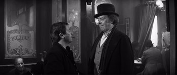 Movie still from “The Elephant Man” (1980), directed by David Lynch – A man in a top hat talking to another man in a suit; Medium shot, Over the shoulder angle