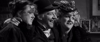 Movie still from “The Elephant Man” (1980), directed by David Lynch – A man and two women wearing hats are smiling for the camera; Close Up shot, Low angle