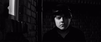 Movie still from “The Elephant Man” (1980), directed by David Lynch – A young man wearing a hat in front of a brick wall; Close Up shot, Low angle