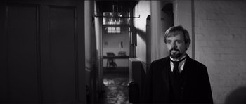 Movie still from “The Elephant Man” (1980), directed by David Lynch – A black and white photo of a man standing in a hallway; Medium shot, Over the shoulder angle