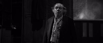 Movie still from “The Elephant Man” (1980), directed by David Lynch – An old man in a black jacket and a white neck tie; Medium shot, Low angle