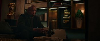 Movie still from “The Enforcer” (2022), directed by Richard Hughes – A man sitting at a table in front of stacks of papers; Medium shot, Low angle