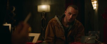 Movie still from “The Enforcer” (2022), directed by Richard Hughes – A man sitting at a table in front of a lamp; Close Up shot, Low angle