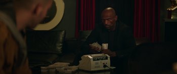 Movie still from “The Enforcer” (2022), directed by Richard Hughes – A man sitting in front of a cash register; Medium shot, Low angle