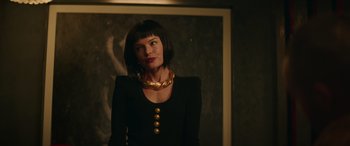 Movie still from “The Enforcer” (2022), directed by Richard Hughes – A woman in a black dress with a gold necklace; Medium shot, Over the shoulder angle