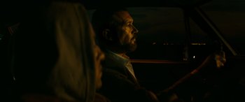 Movie still from “The Enforcer” (2022), directed by Richard Hughes – A man and a woman sitting in a car at night; Medium shot, Low angle