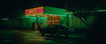 Movie still from “The Enforcer” (2022), directed by Richard Hughes – A car parked in front of a neon lit motel; Wide shot, Low angle