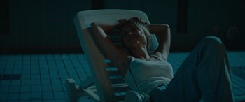 Movie still from “The Enforcer” (2022), directed by Richard Hughes – A woman laying on a lounge chair at night; Medium shot, High angle
