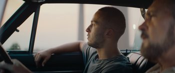 Movie still from “The Enforcer” (2022), directed by Richard Hughes – A man sitting in the back seat of a car looking out the window; Close Up shot, Low angle