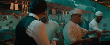 Movie still from “The Enforcer” (2022), directed by Richard Hughes – A group of men standing around in a kitchen; Medium shot, Over the shoulder angle