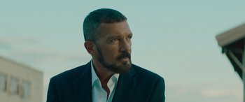 Movie still from “The Enforcer” (2022), directed by Richard Hughes – A person wearing a suit and beard; Close Up shot, Low angle