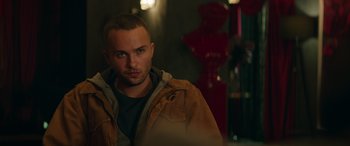 Movie still from “The Enforcer” (2022), directed by Richard Hughes – A man in a brown jacket is looking at the camera; Close Up shot, Over the shoulder angle