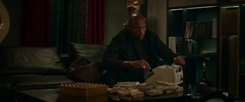 Movie still from “The Enforcer” (2022), directed by Richard Hughes – A man sitting at a table with a lot of money in front of him; Medium shot, Low angle