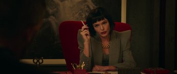 Movie still from “The Enforcer” (2022), directed by Richard Hughes – A woman sitting at a table smoking a cigarette; Medium shot, Over the shoulder angle