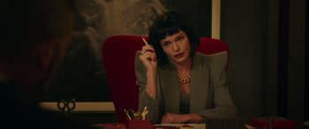 Movie still from “The Enforcer” (2022), directed by Richard Hughes – A woman sitting at a table smoking a cigarette; Medium shot, Over the shoulder angle