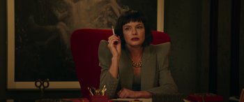 Movie still from “The Enforcer” (2022), directed by Richard Hughes – A woman sitting at a table smoking a cigarette; Medium shot, Over the shoulder angle