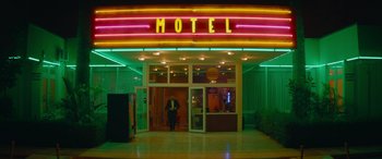 Movie still from “The Enforcer” (2022), directed by Richard Hughes – A man standing in front of a neon hotel sign; Extreme Wide shot, Low angle