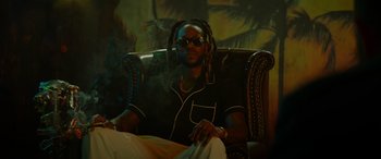 Movie still from “The Enforcer” (2022), directed by Richard Hughes – A man sitting in a chair smoking a cigarette; Medium shot, Low angle