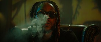 Movie still from “The Enforcer” (2022), directed by Richard Hughes – A man with dreads and sunglasses smoking a cigarette; Close Up shot, Low angle