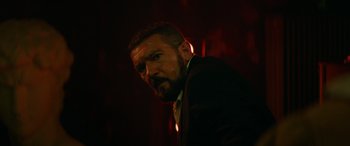Movie still from “The Enforcer” (2022), directed by Richard Hughes – A man in a suit and tie in a dark room; Close Up shot, Low angle