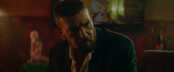 Movie still from “The Enforcer” (2022), directed by Richard Hughes – A person wearing a suit and beard; Close Up shot, Low angle